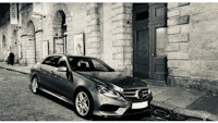 a black and white photo of a mercedes e class parked on a cobblestone street